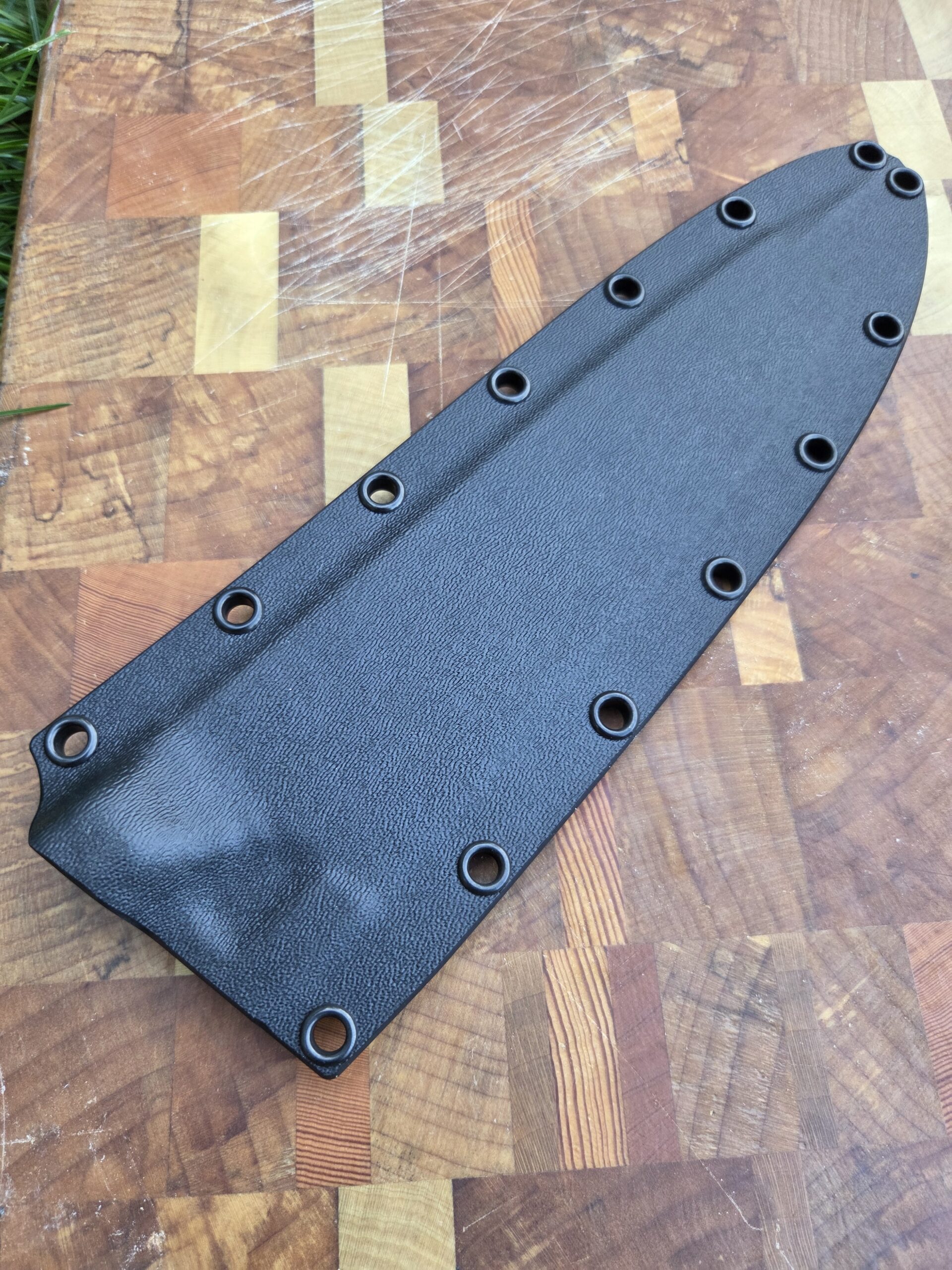 8" chef knife sheath on cutting board. Black kydex with black eyelets